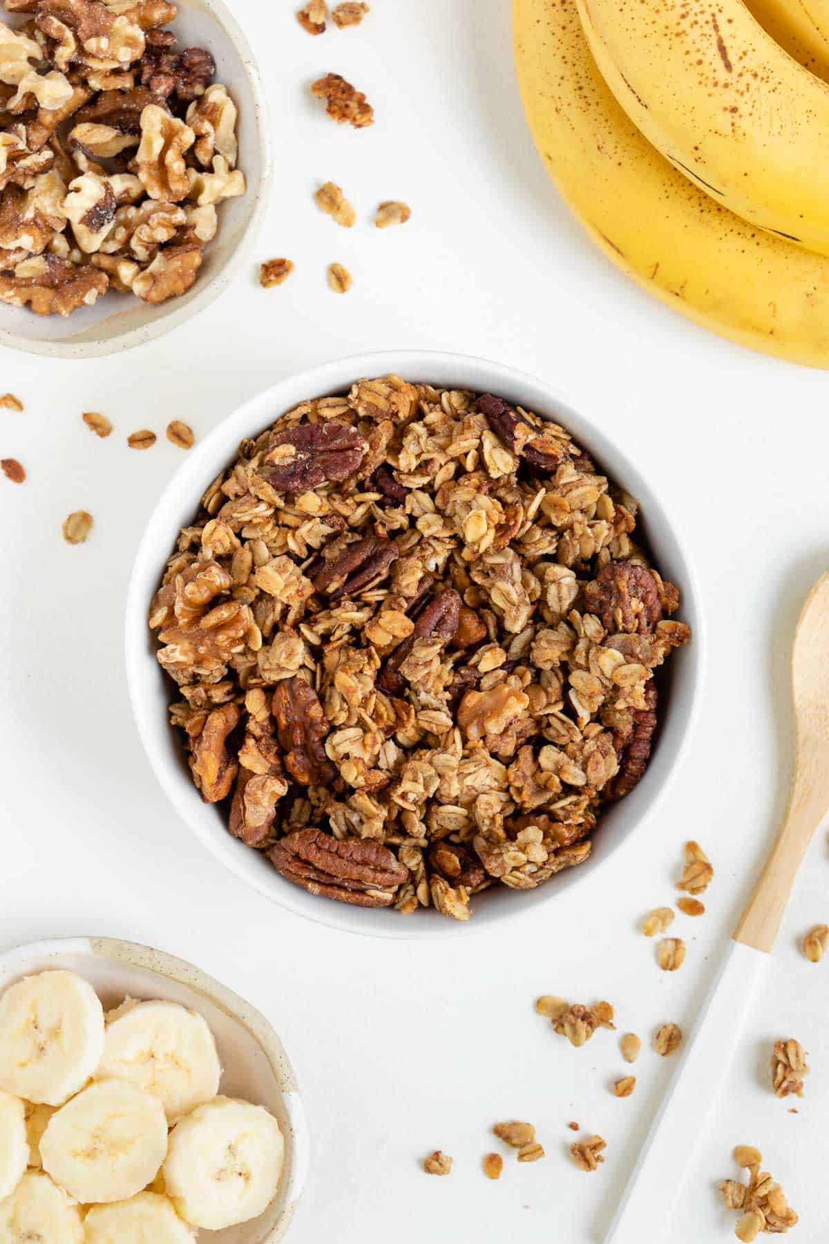 banana bread granola inside a white bowl surrounded by walnuts, sliced banana, and banana peels