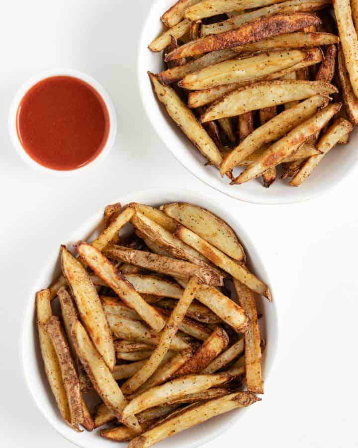 two white bowls filled with crispy baked french fries beside a bowl of ketchup