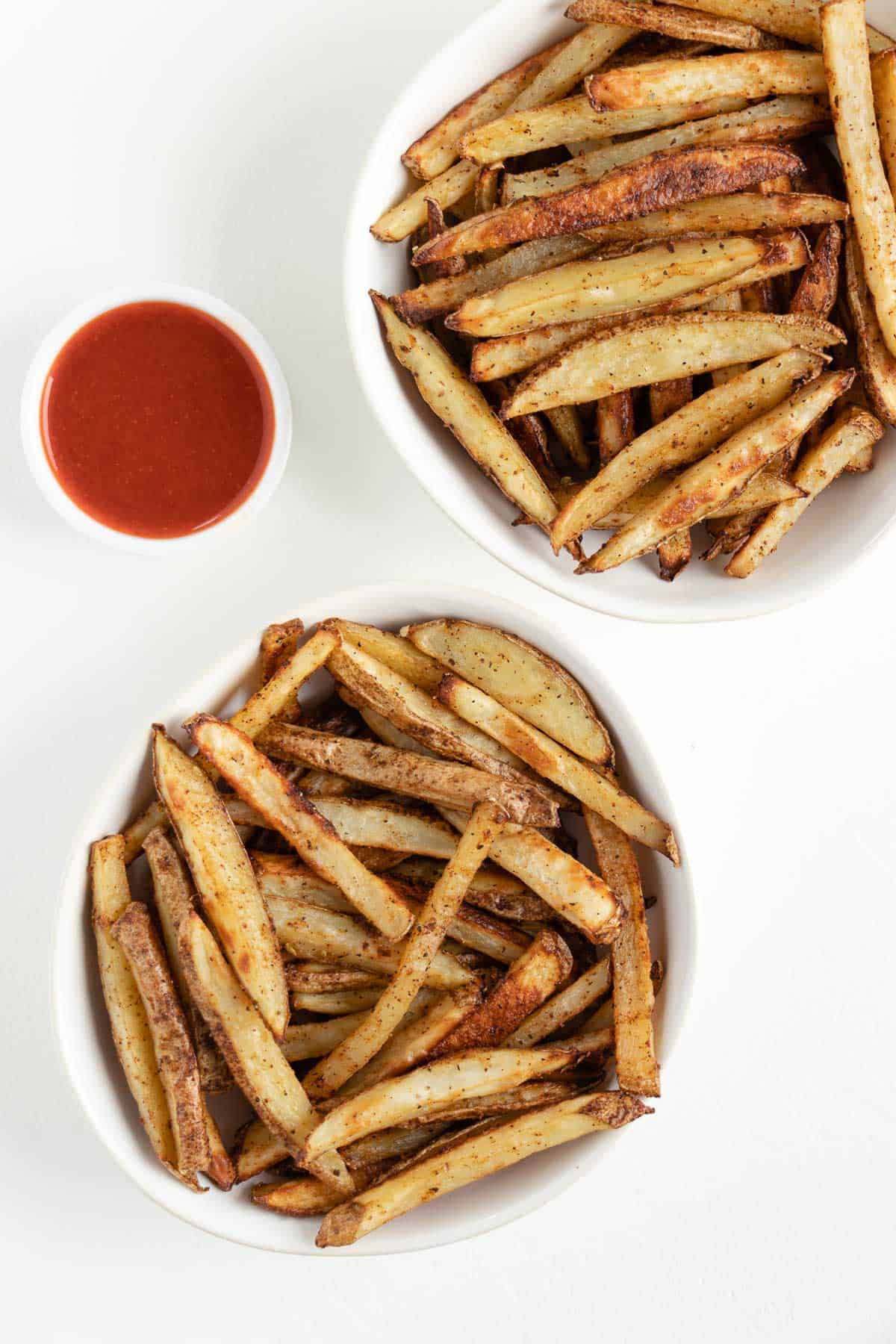 two white bowls filled with crispy baked french fries beside a bowl of ketchup