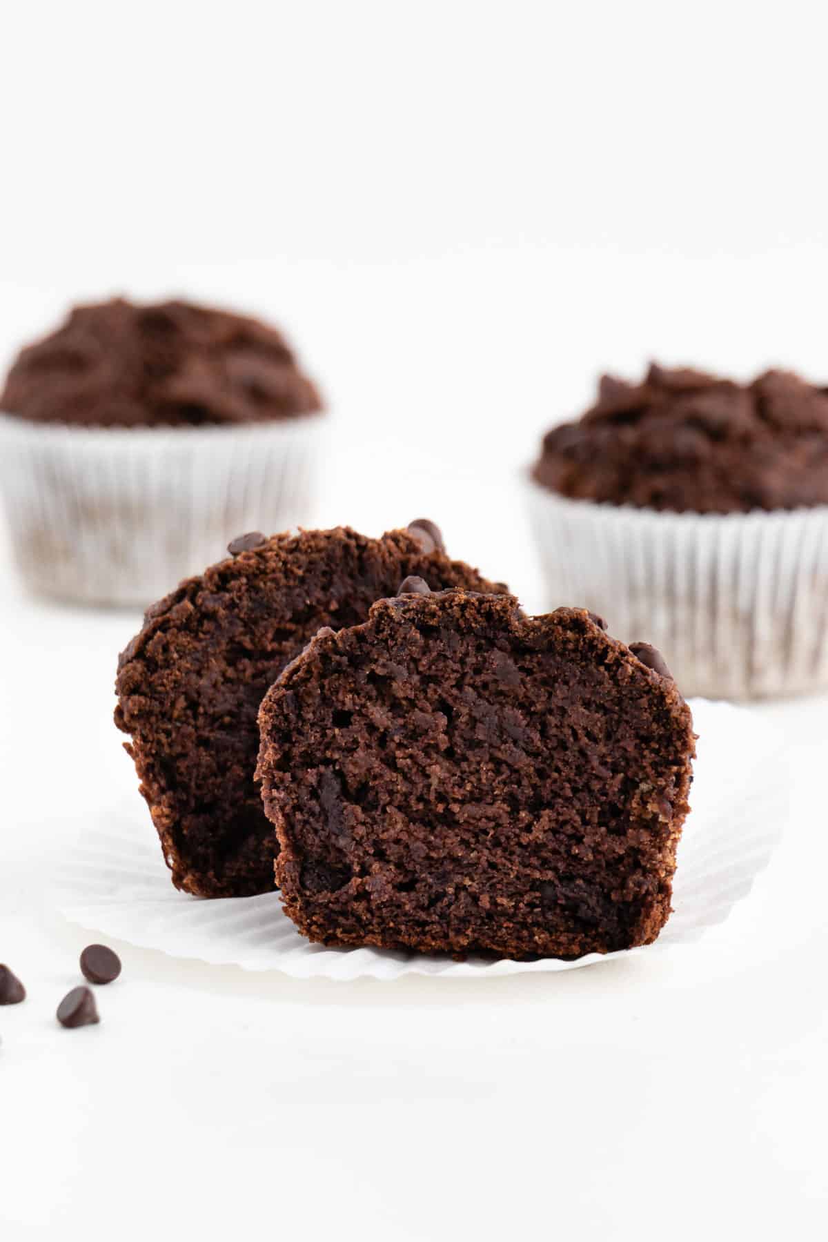 a sliced double chocolate banana muffin in front of two whole muffins