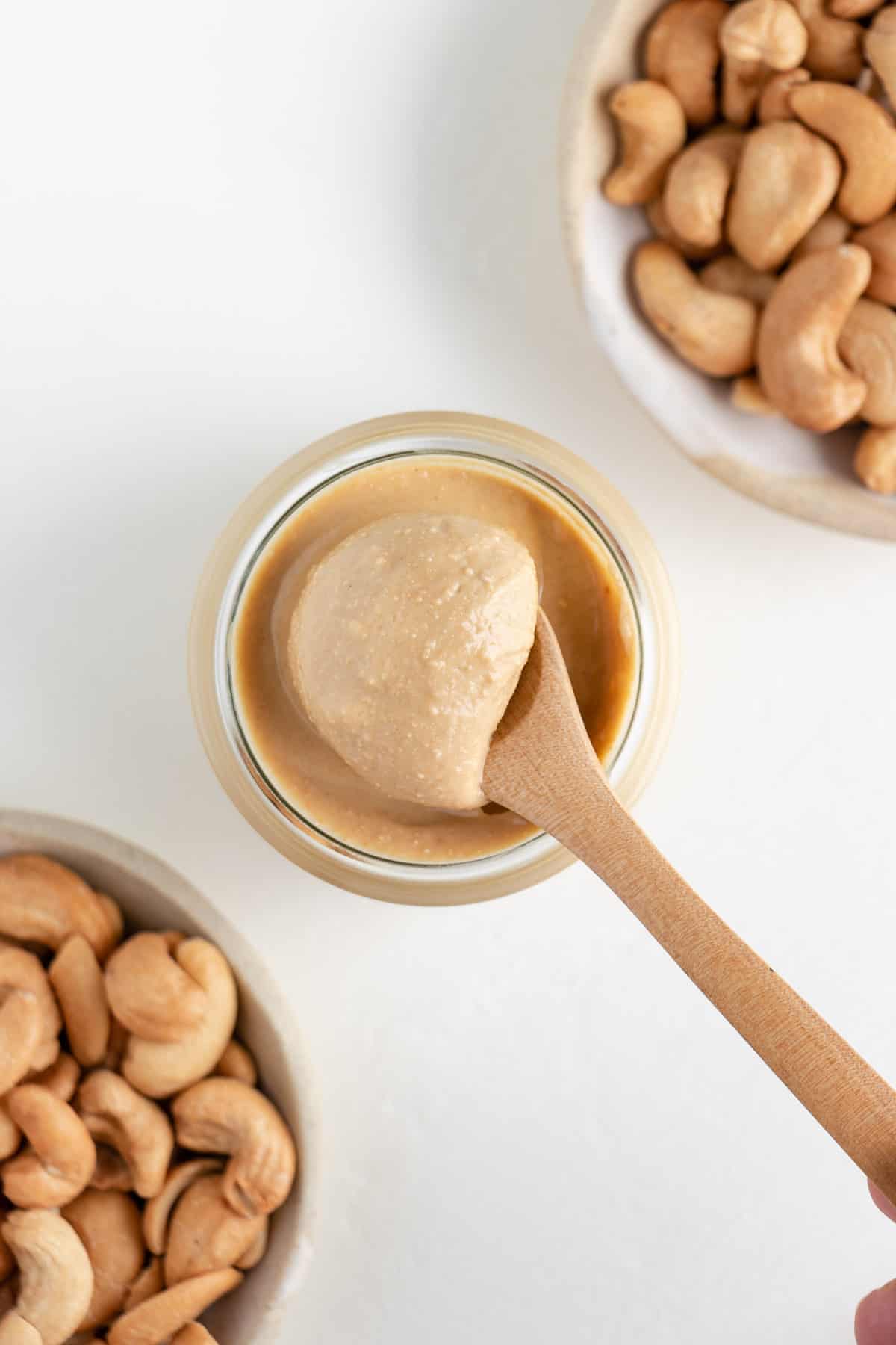 a wooden spoon scooping cashew butter out of a glass jar