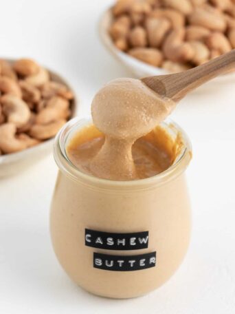 a wooden spoon scooping cashew butter out of a glass jar