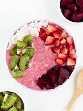 strawberry beet smoothie bowl beside a wooden spoon and bowl of kiwi