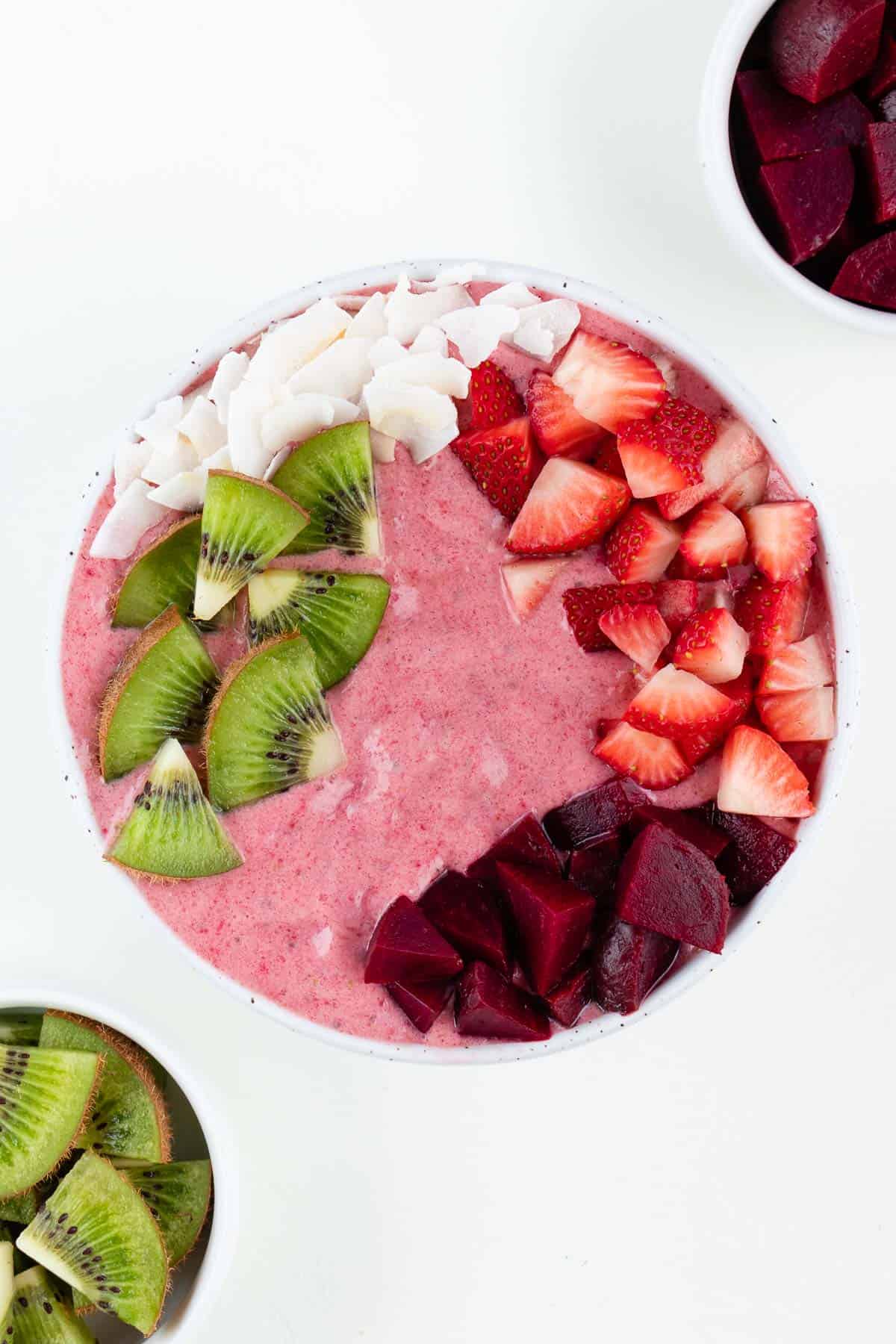 strawberry beet smoothie bowl topped with coconut flakes, kiwi fruit, strawberries, and beets