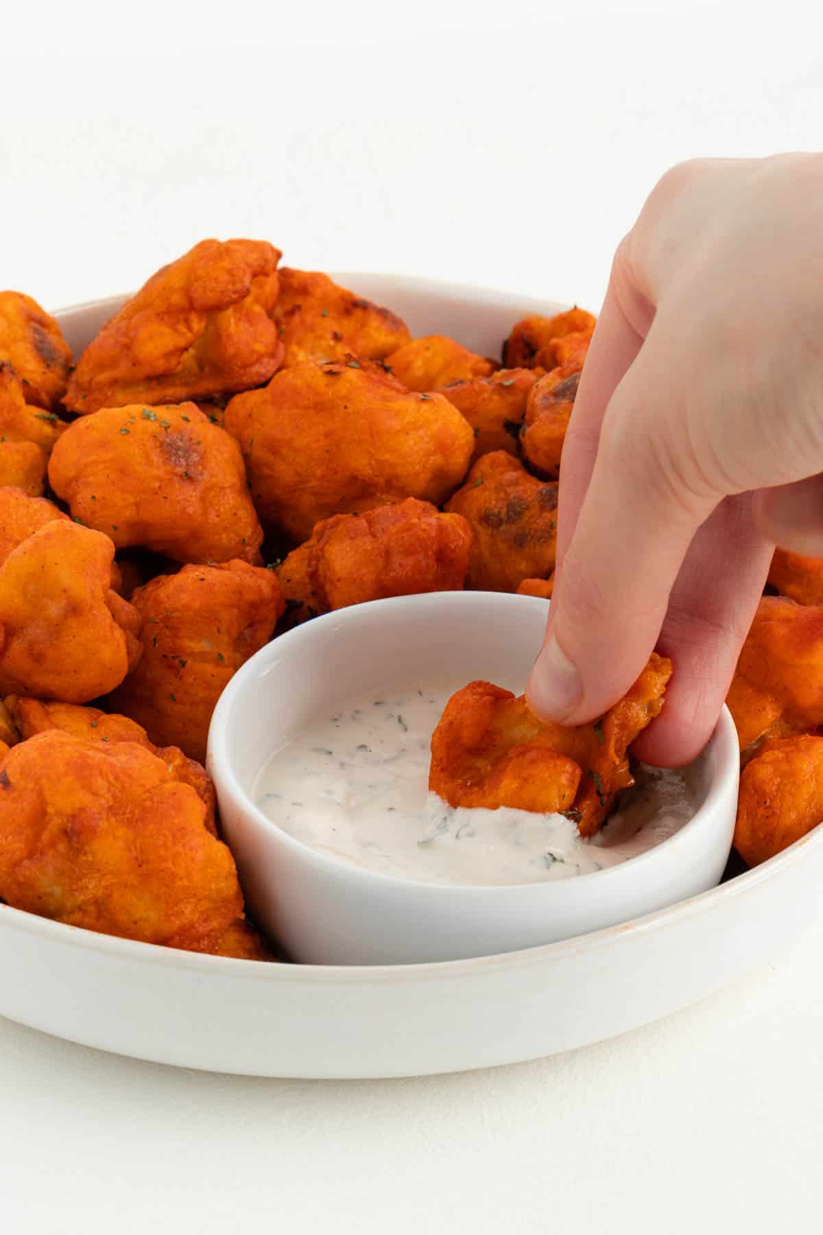 a hand dipping a vegan buffalo cauliflower wing into a bowl of ranch dressing