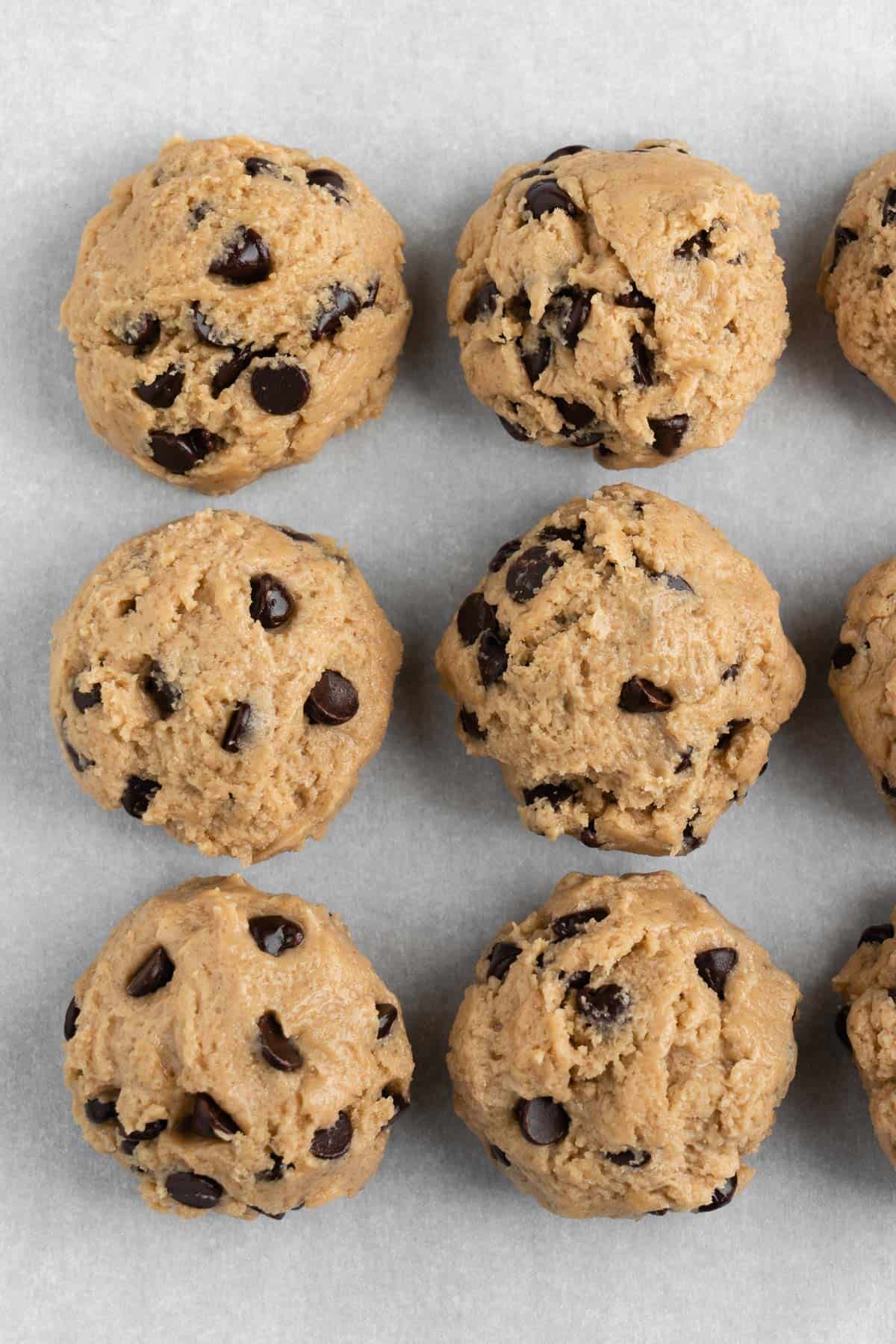 six round scoops of chocolate chip cookie dough on a baking sheet