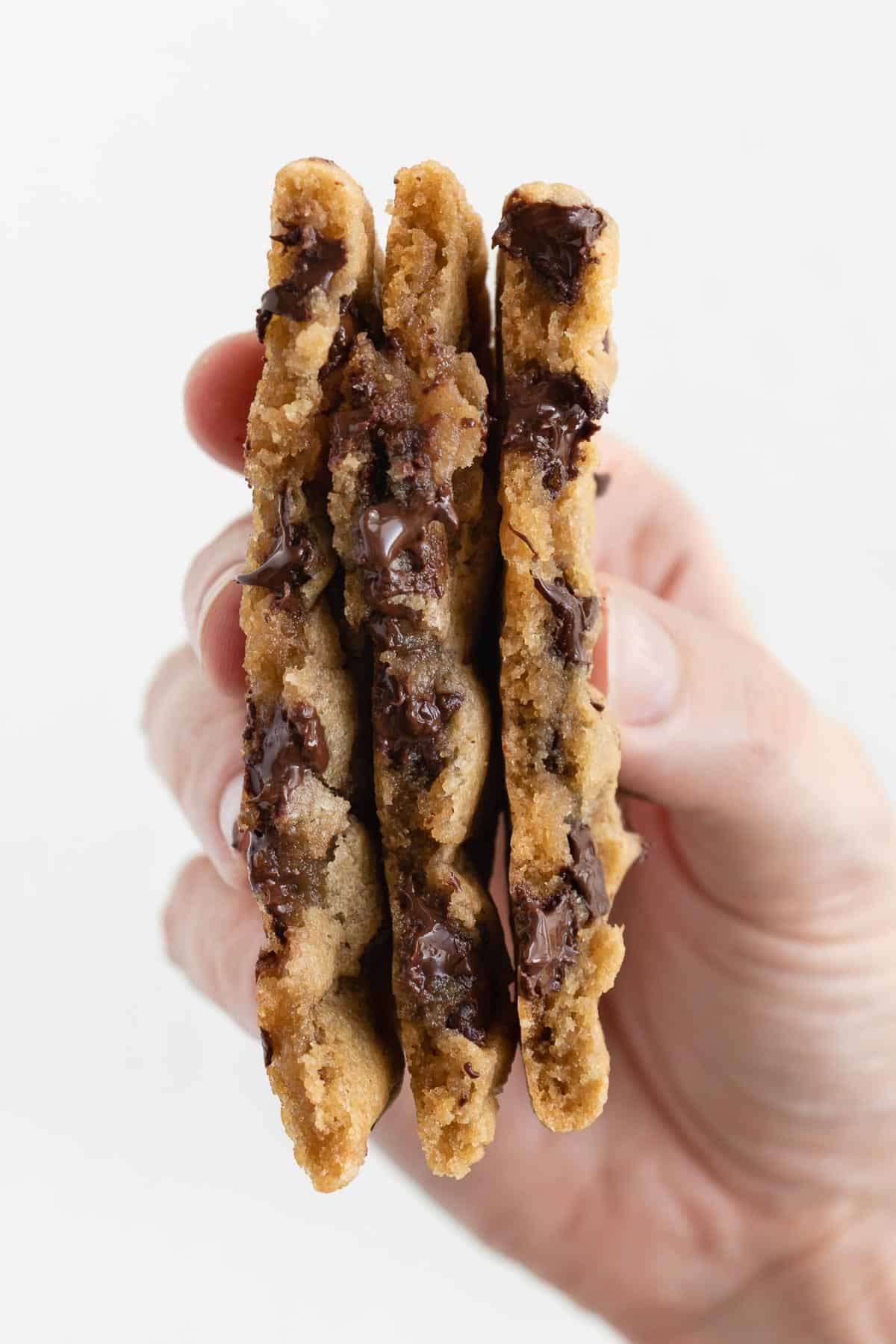 a hand holding three halves of gooey chocolate chip cookies