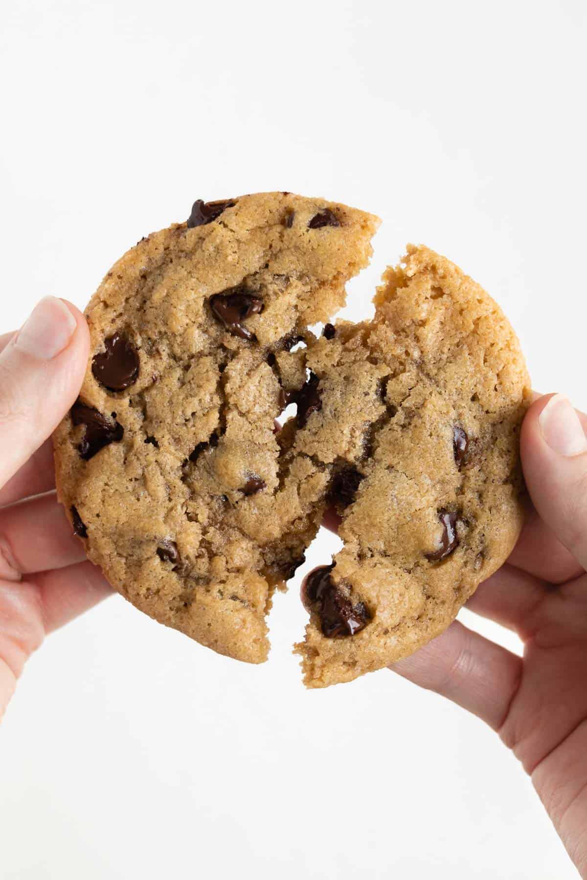 two hands pulling apart a warm and gooey vegan chocolate chip cookie