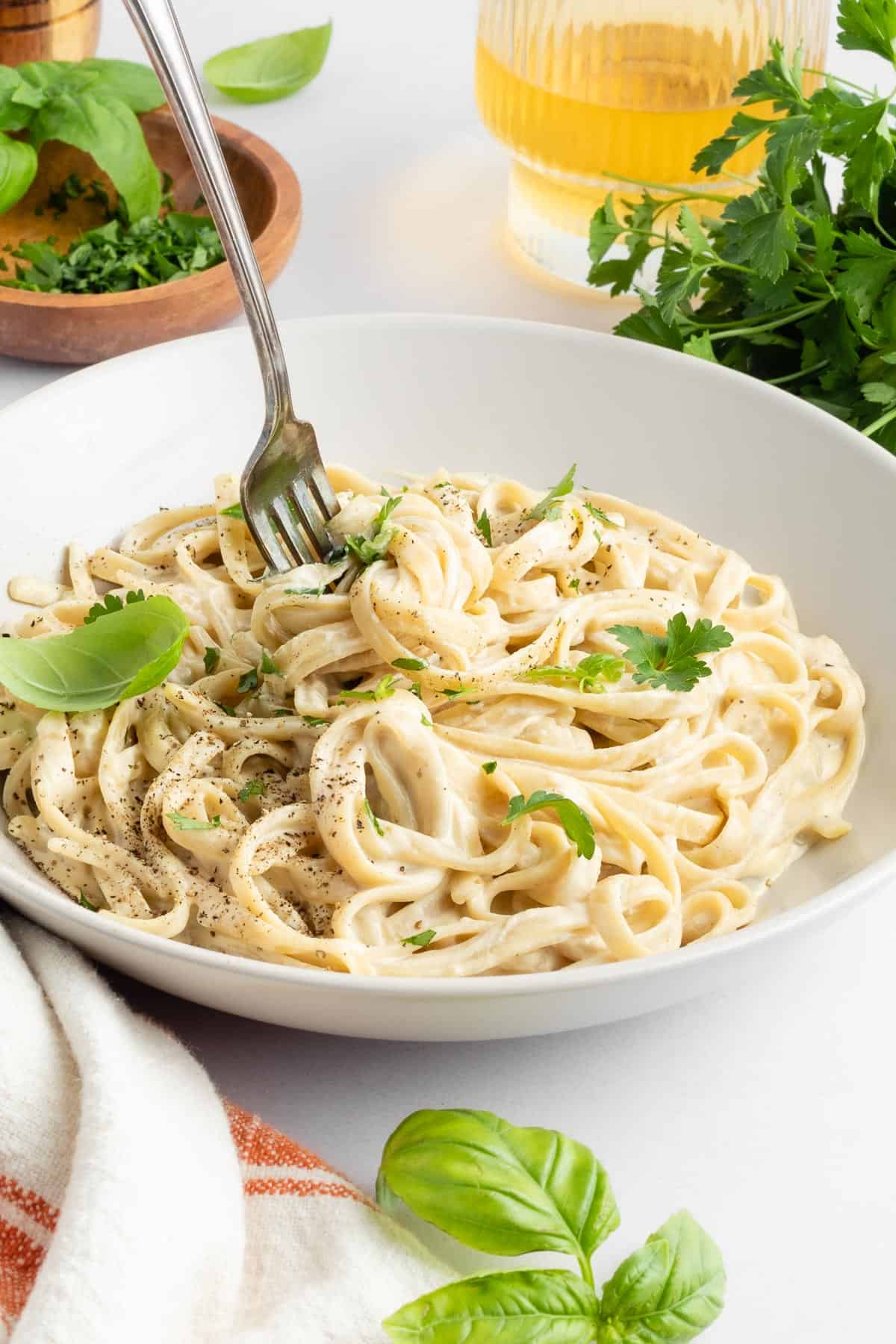 vegan fettuccine alfredo pasta inside two white bowls beside cashews and a wooden fork