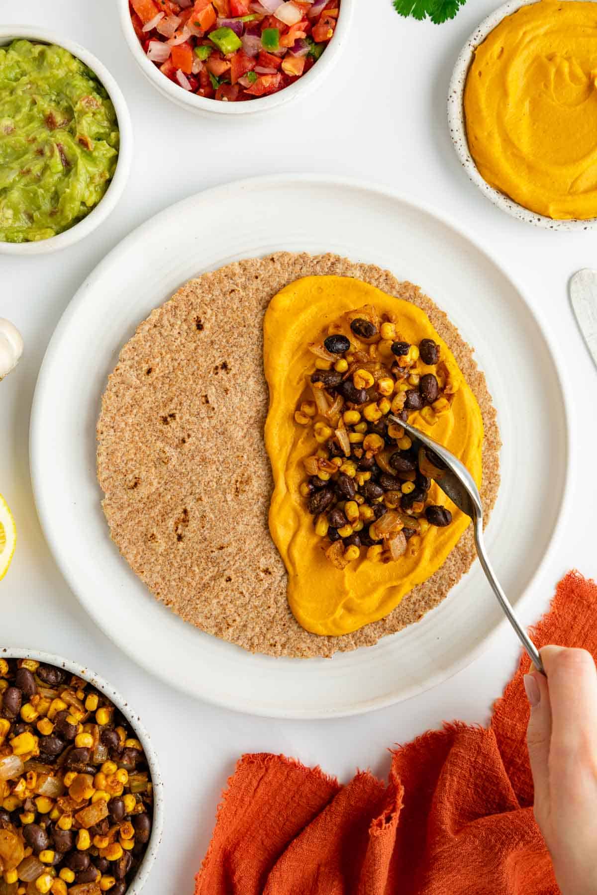 a hand spooning black beans and corn on the cheese layer for a vegan quesadilla