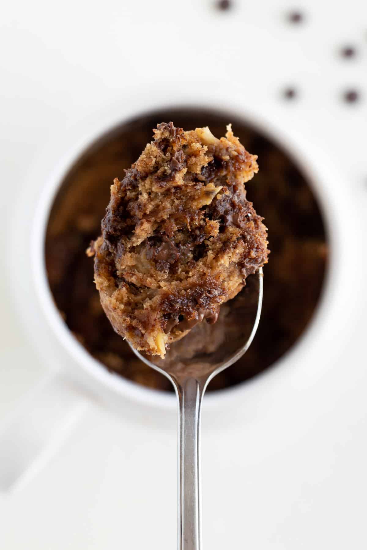 a spoonful of vegan chocolate chip mug cake being held over a white mug