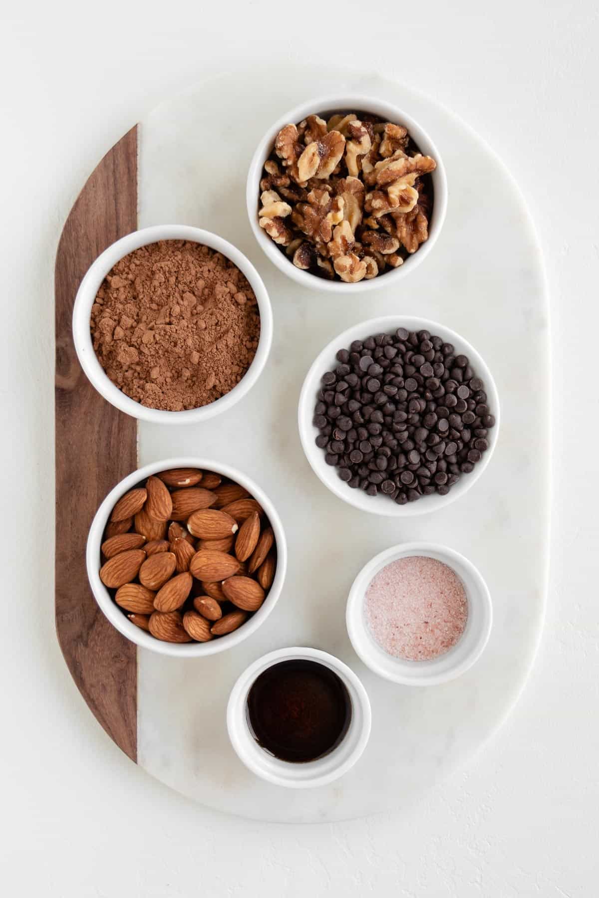 small bowls of walnuts, almonds, cacao powder, chocolate chips, vanilla, and salt on a marble board