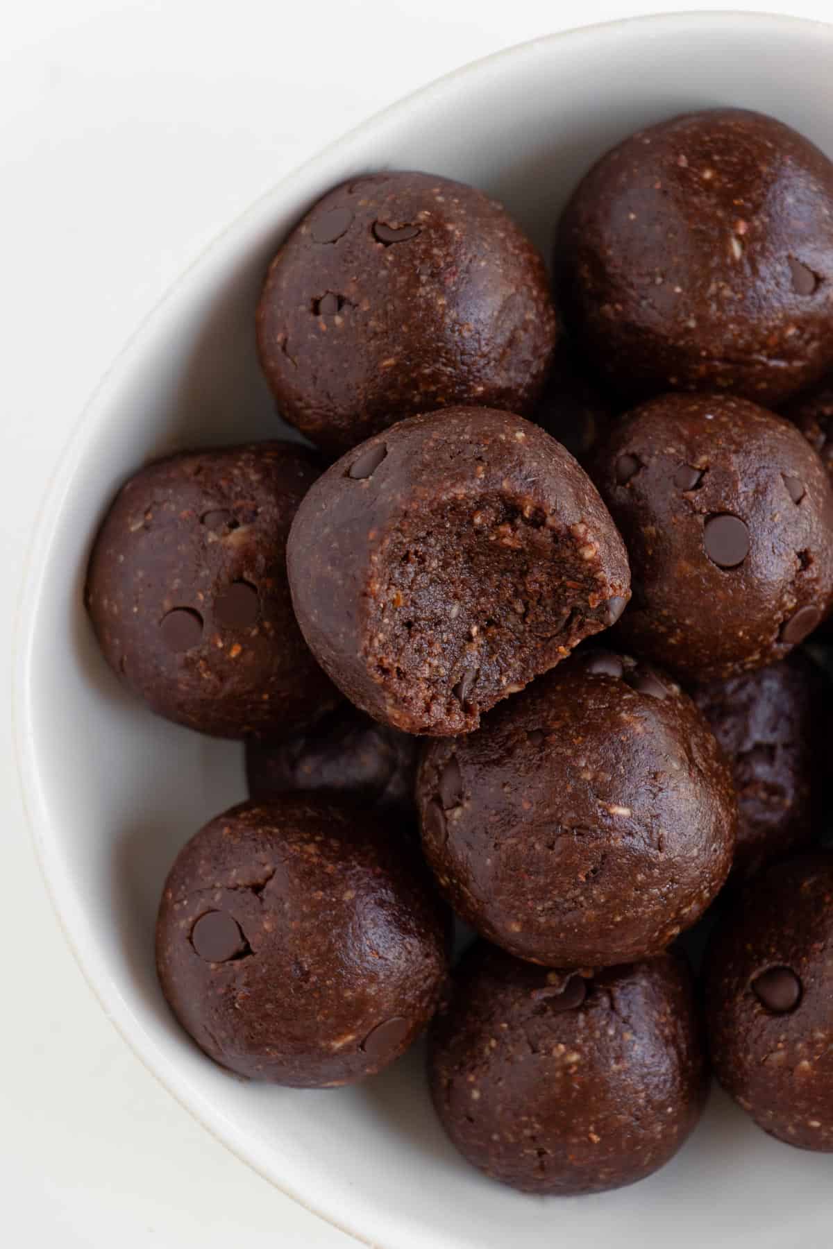 chocolate bliss balls in a white bowl with a bite taken out of the center one