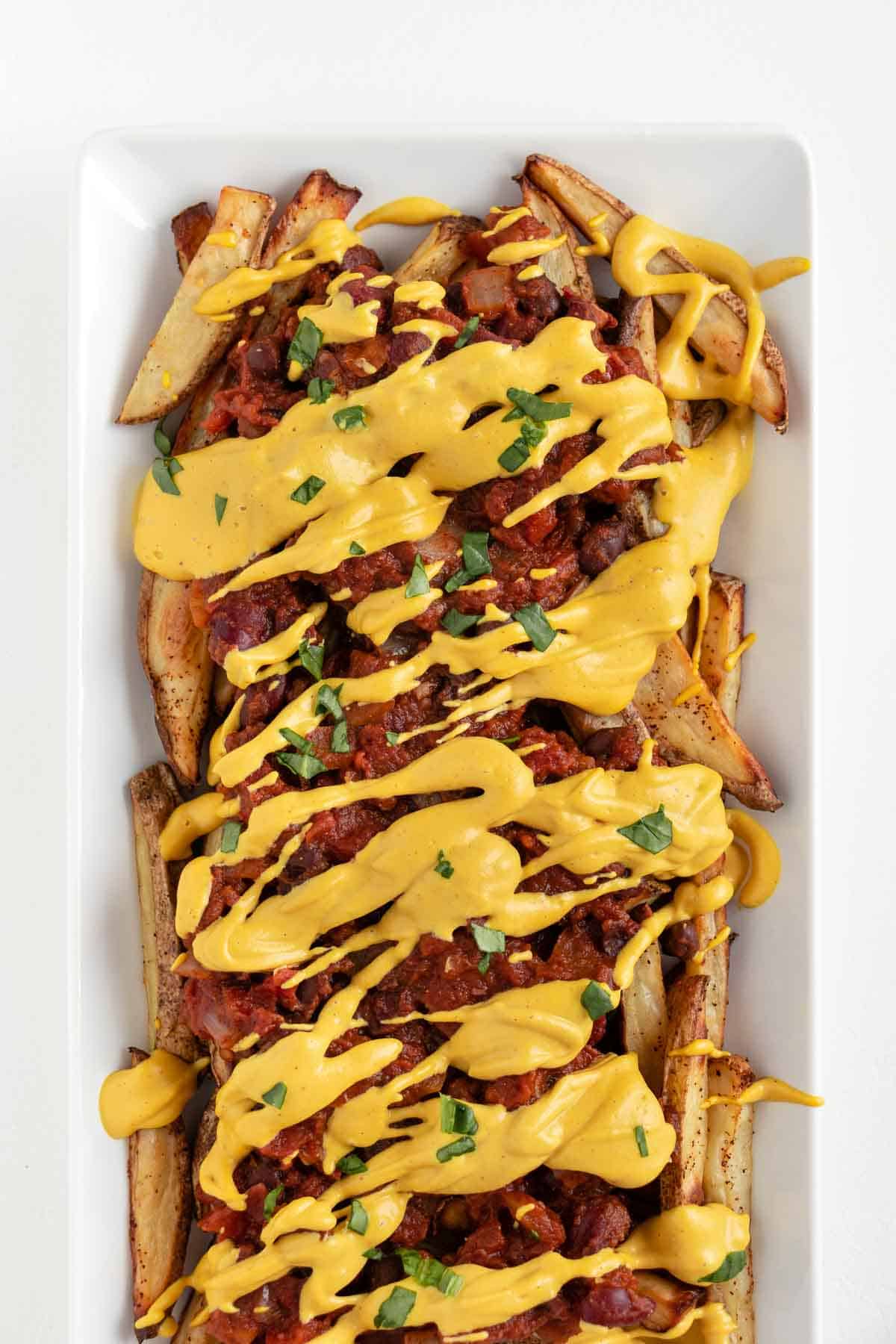 vegan chili cheese fries on a white rectangular plate