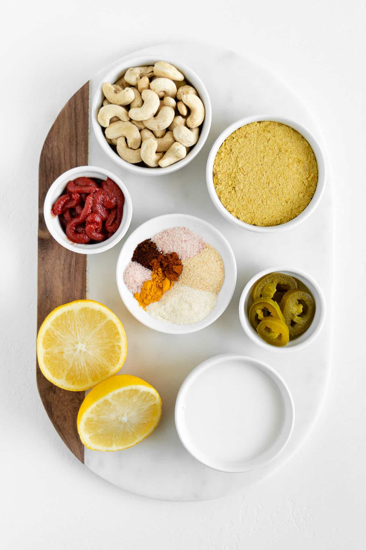 a sliced lemon, raw cashews, jalapeño, spices, tomato paste, almond milk, and nutritional yeast on a marble board