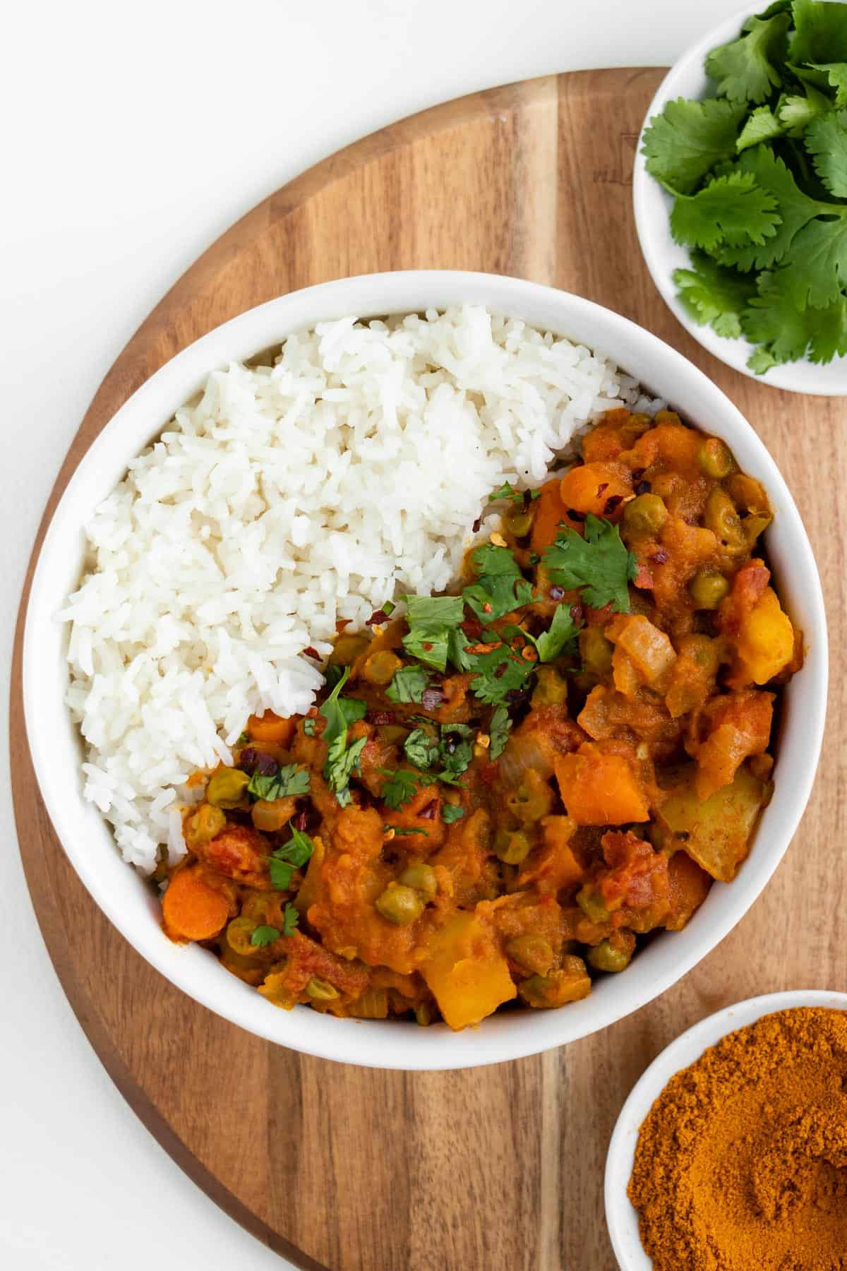 vegan batata curry dentro de uma tigela branca em uma rodada de madeira de bordo