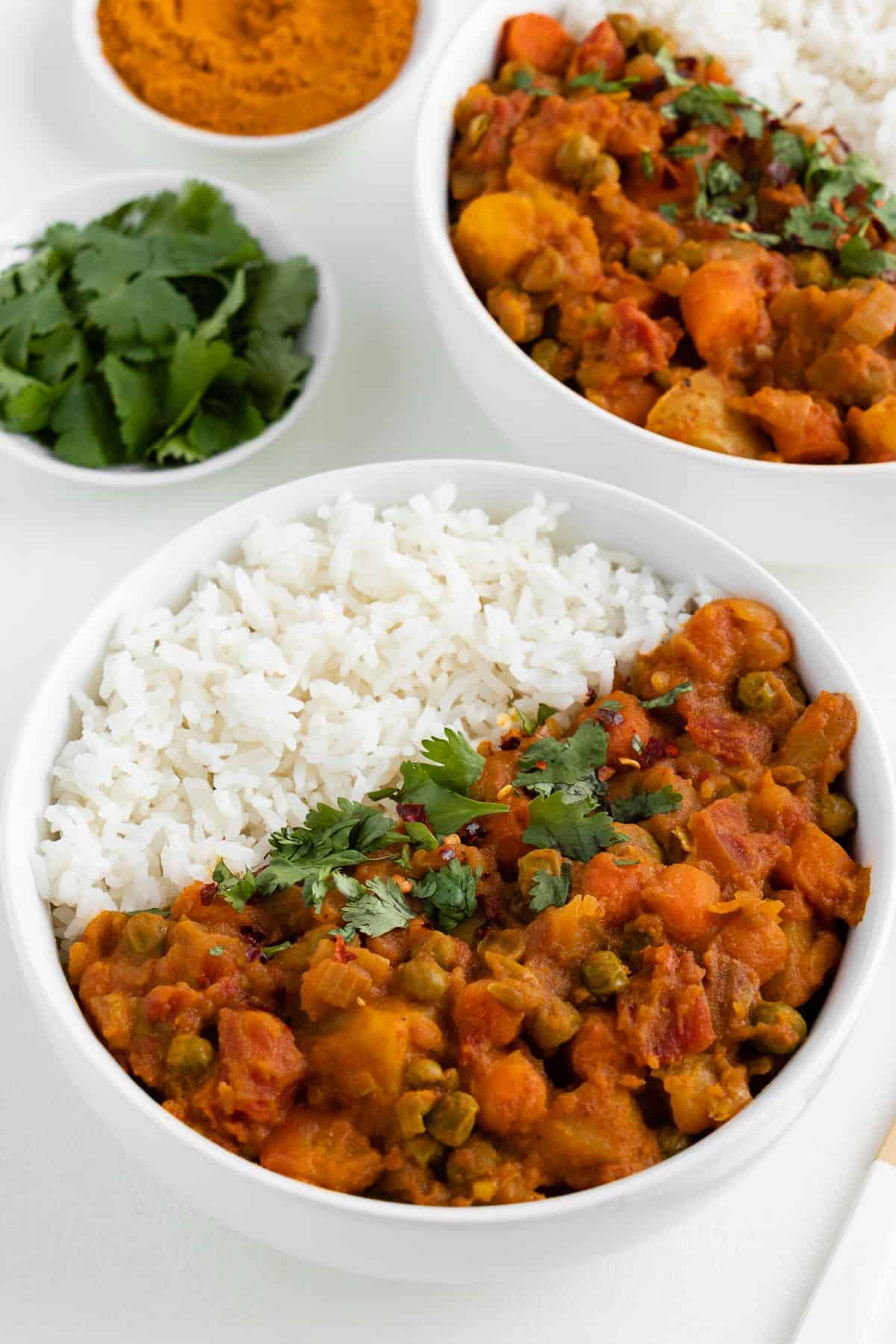 veganistische aardappelcurry in een witte kom met jasmijnrijst en koriander