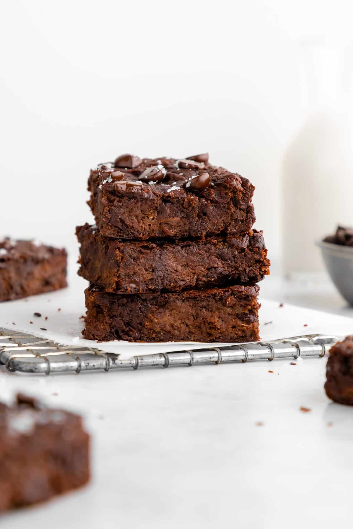 a stack of four flourless vegan protein brownies in front of a bowl of chocolate chips and a bowl of chocolate protein powder