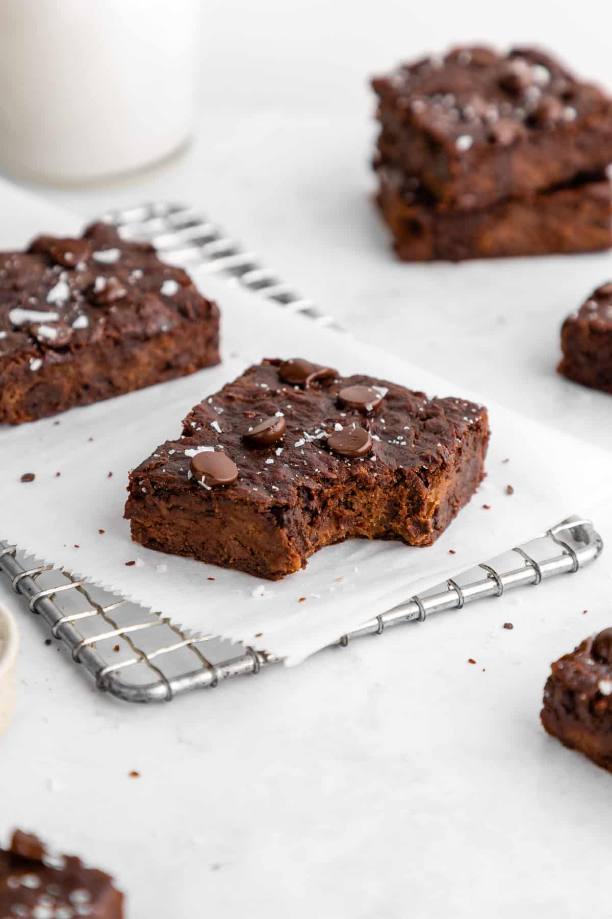 a vegan protein brownie with a bite taken out of it surrounded by chocolate chips and a bowl of chocolate protein powder