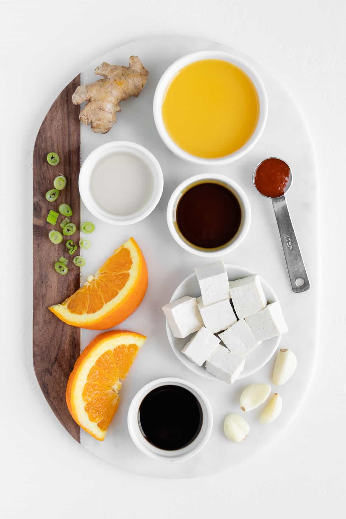 a marble board topped with fruit, a glass of juice, maple syrup, soy sauce, ginger, and green onion