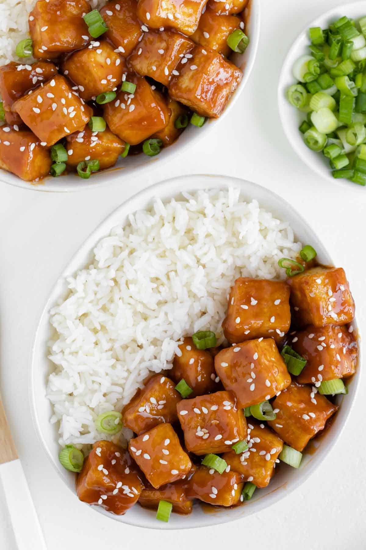 two bowls filled with white rice and crispy baked orange tofu