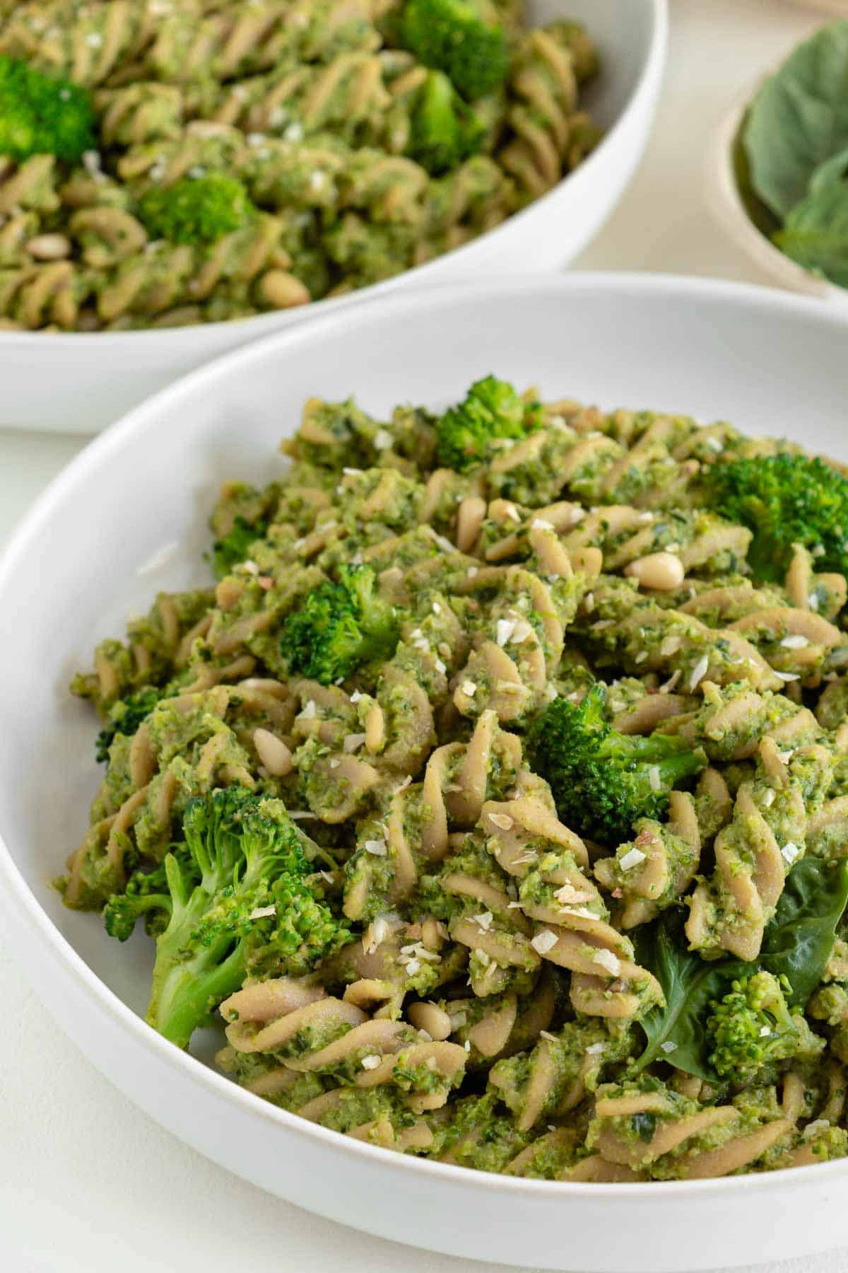 vegan broccoli pesto pasta inside a large white bowl with pine nuts and broccoli