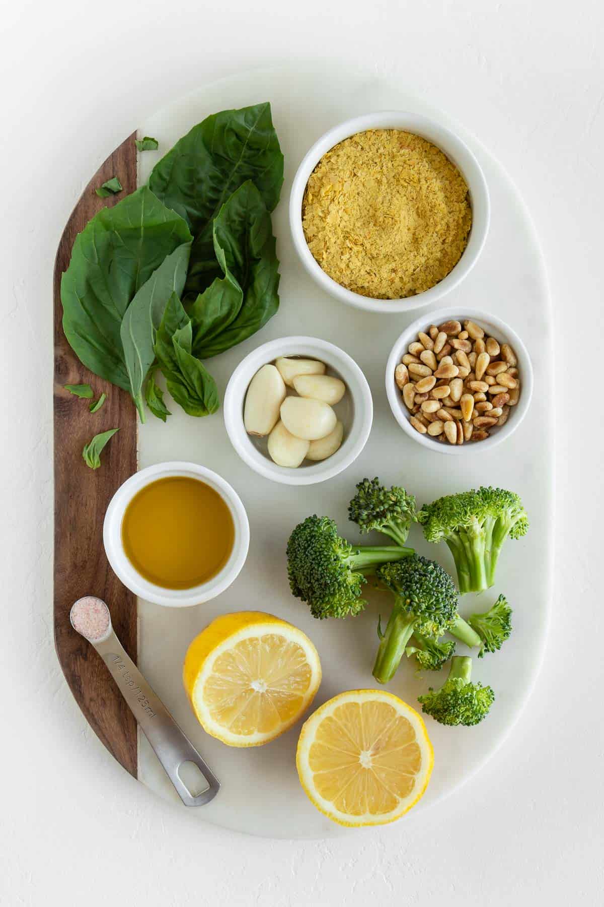 basil, pine nuts, garlic cloves, lemon, olive oil, nutritional yeast, and salt on a white marble board