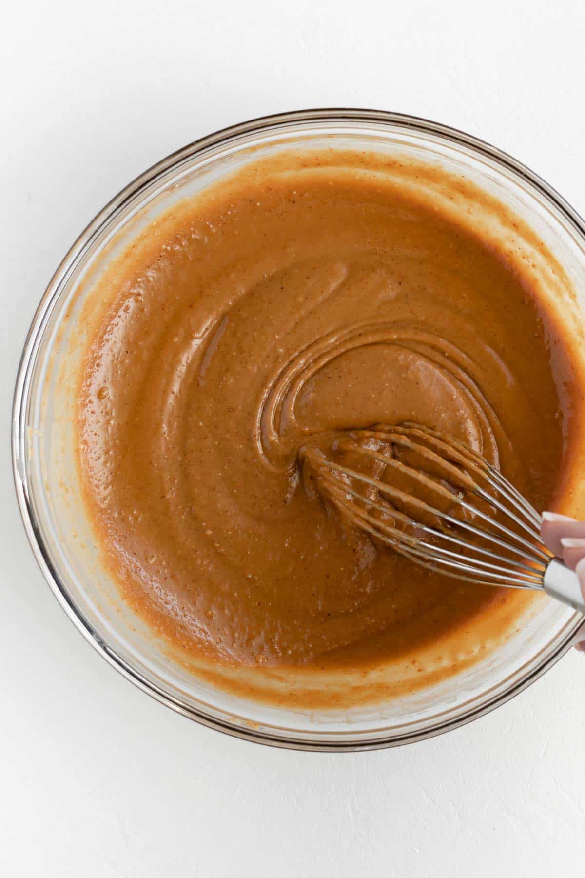a hand whisking peanut sauce in a glass bowl