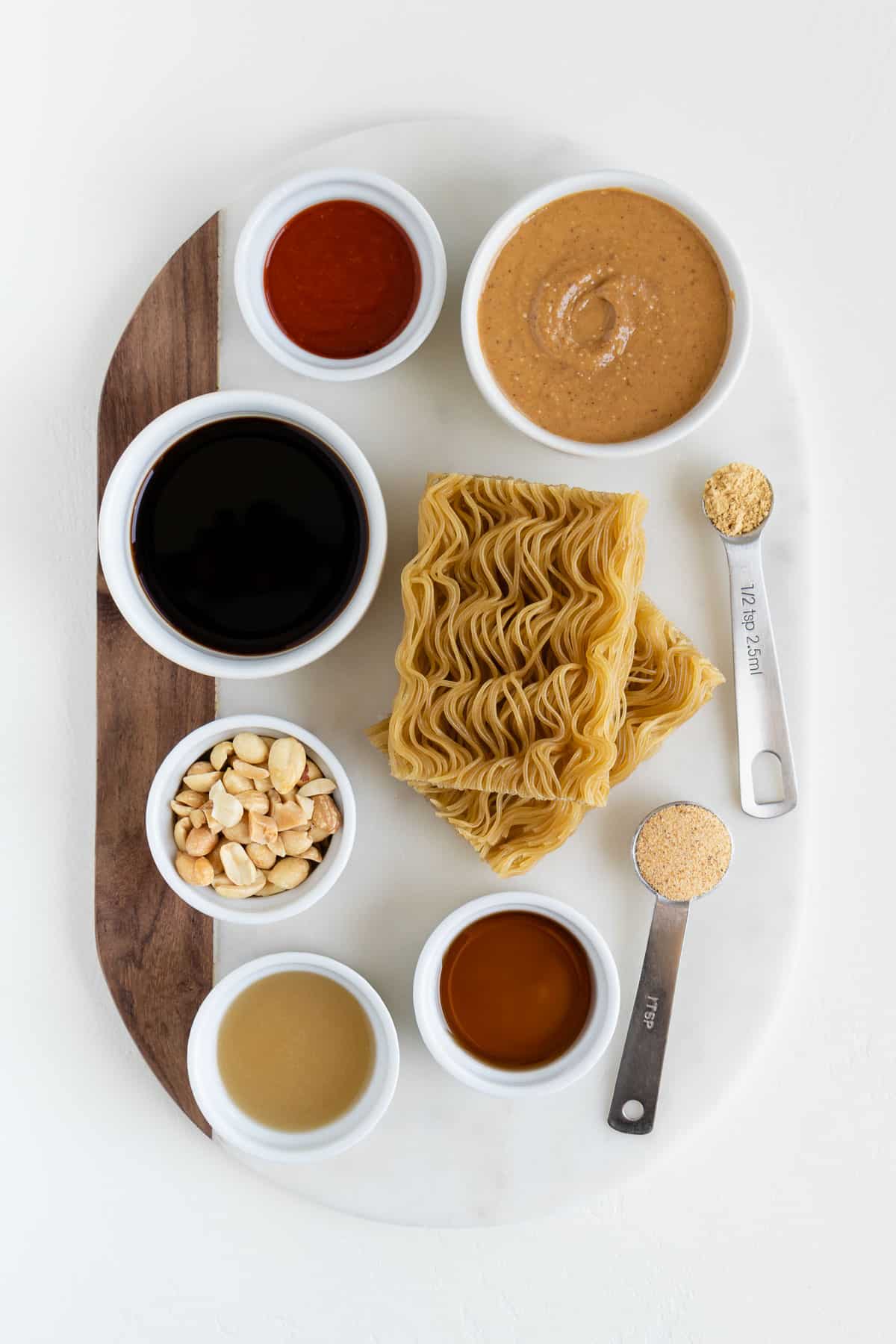 brown rice ramen noodles, soy sauce, maple syrup, chopped nuts, lime juice, sriracha, garlic powder, and ground ginger on a marble board