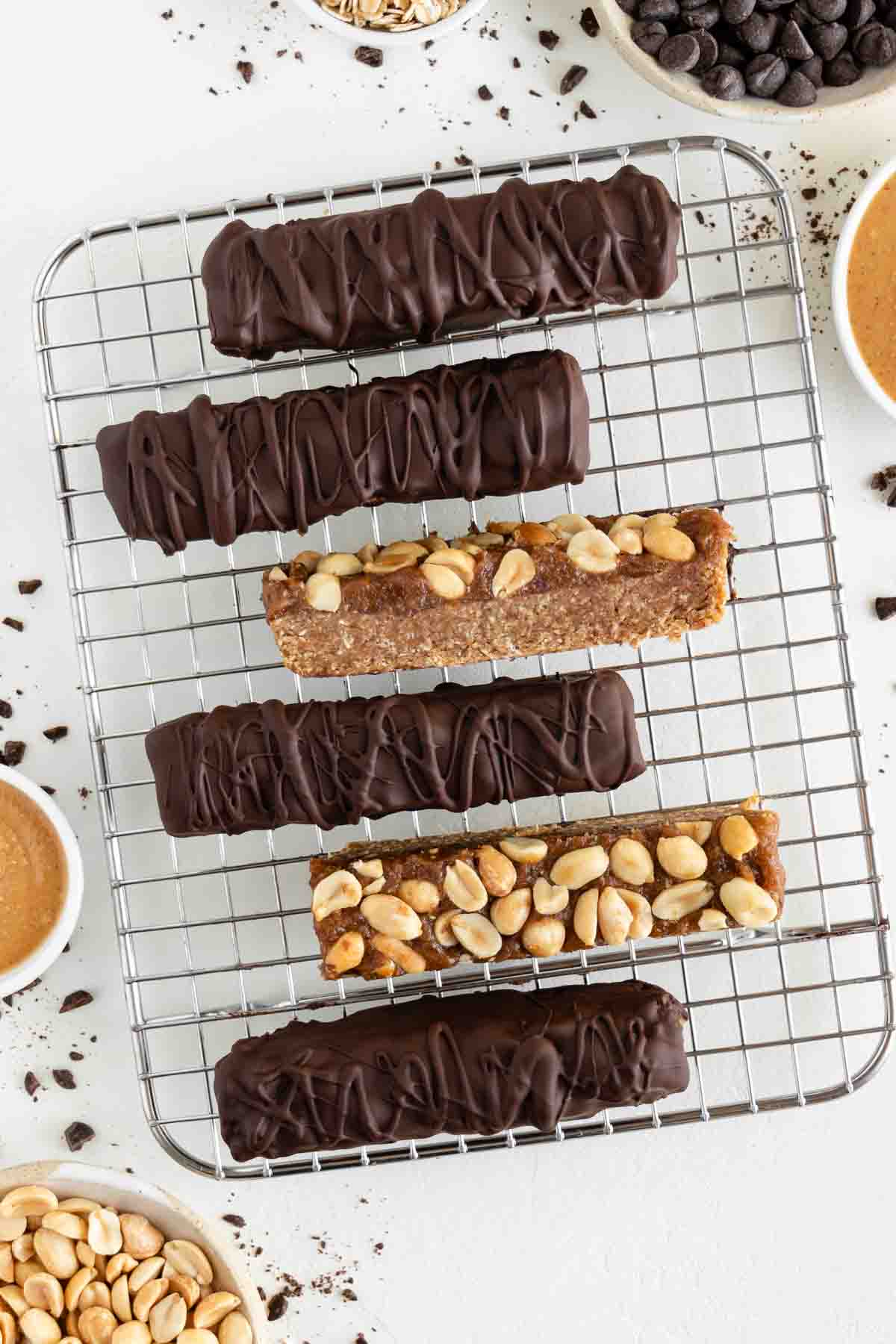 vegan snickers bars on a wire rack surrounded by chocolate chips, medjool dates, peanut butter, and rolled oats