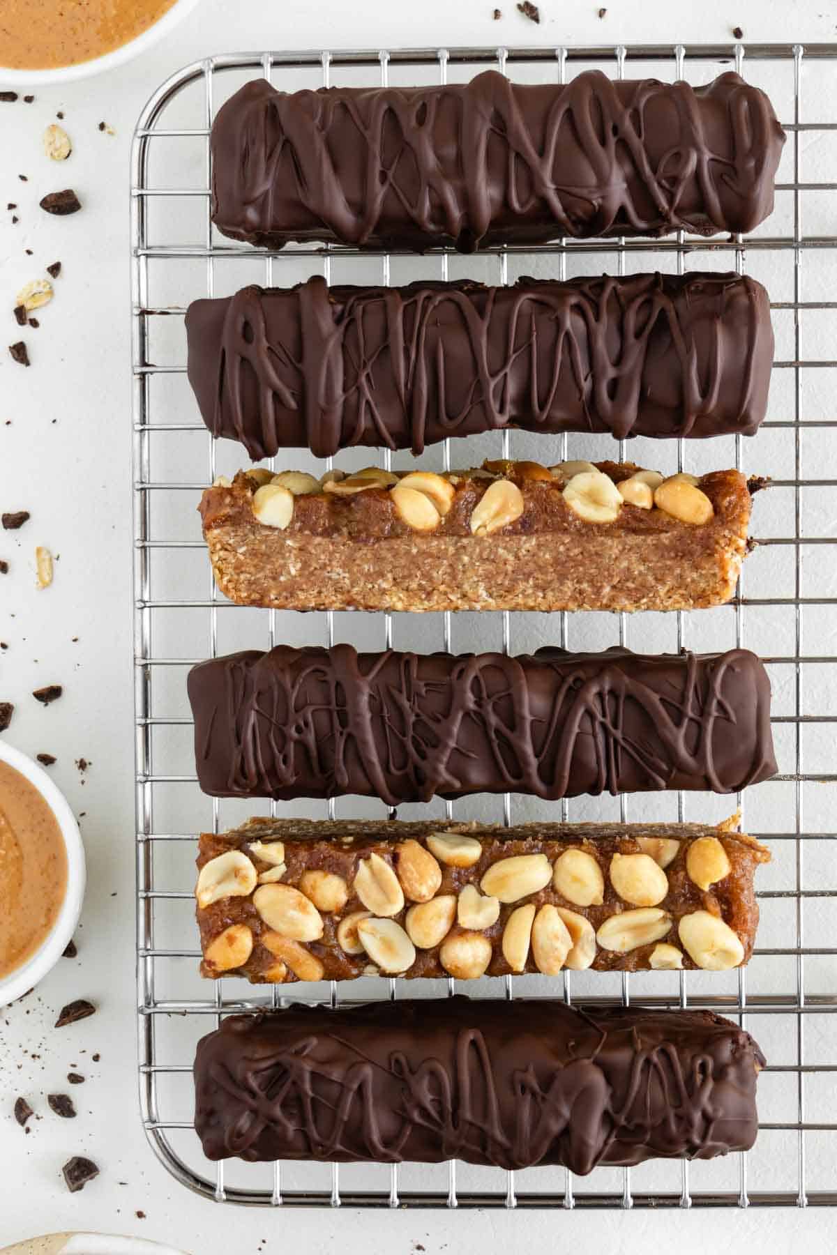 vegan snickers bars on a wire rack surrounded by chocolate chips, medjool dates, peanut butter, and rolled oats