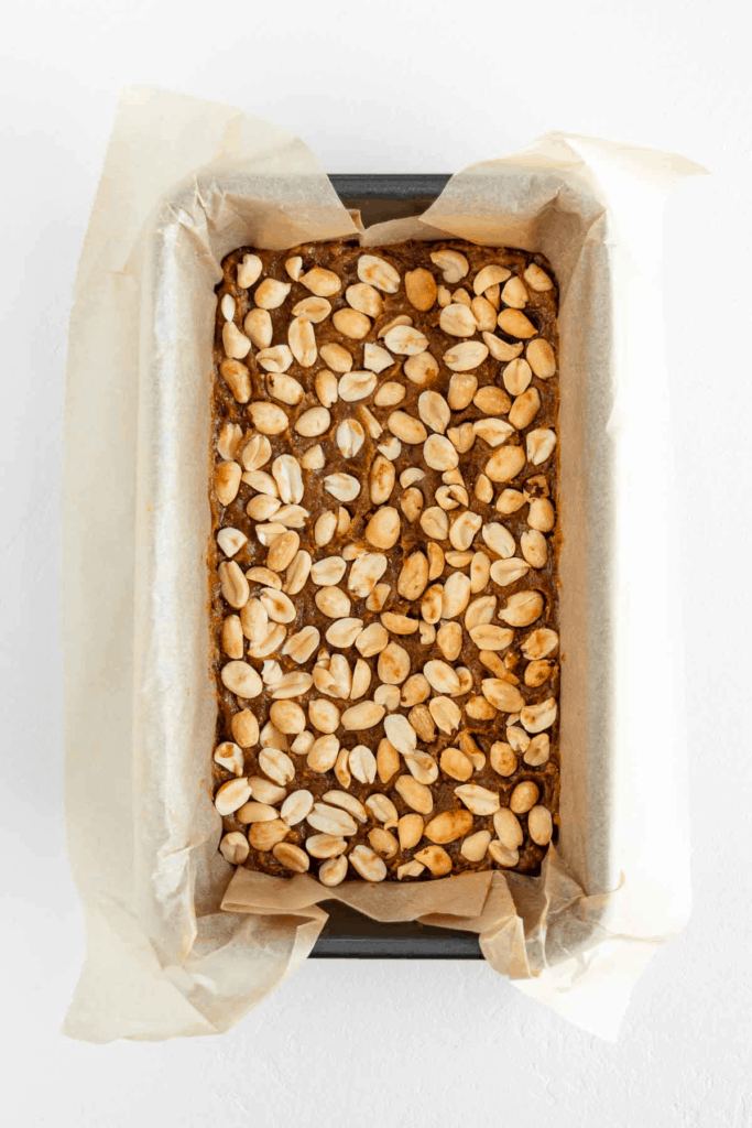a hand spreading vegan nougat and date caramel into a loaf pan