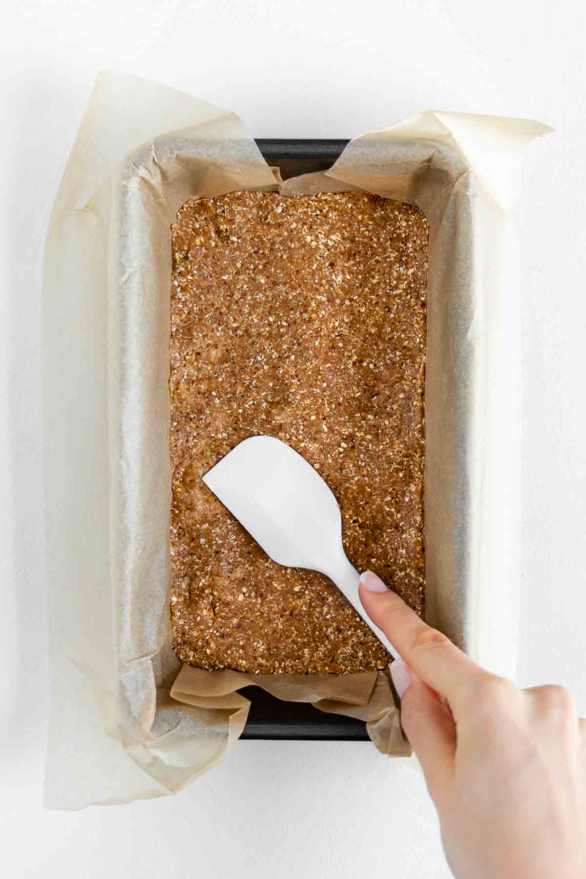 a hand holding a white spatula pressing vegan nougat into a loaf pan