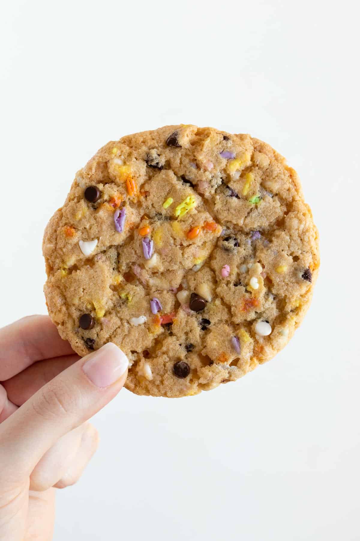 a hand holding a giant vegan birthday cake cookie with sprinkles, white chocolate chips, and chocolate chips