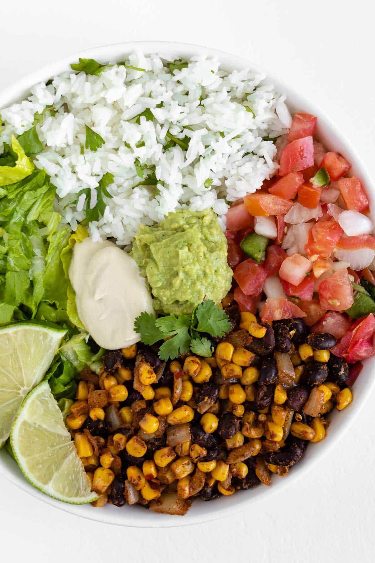 vegan burrito bowl with black beans, corn, cilantro lime rice, pico de gallo, lettuce, guacamole, and cashew sour cream