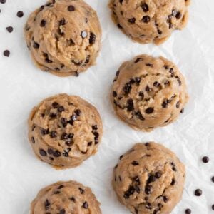six large scoops of edible vegan cookie dough on white parchment paper surrounded by chocolate chips