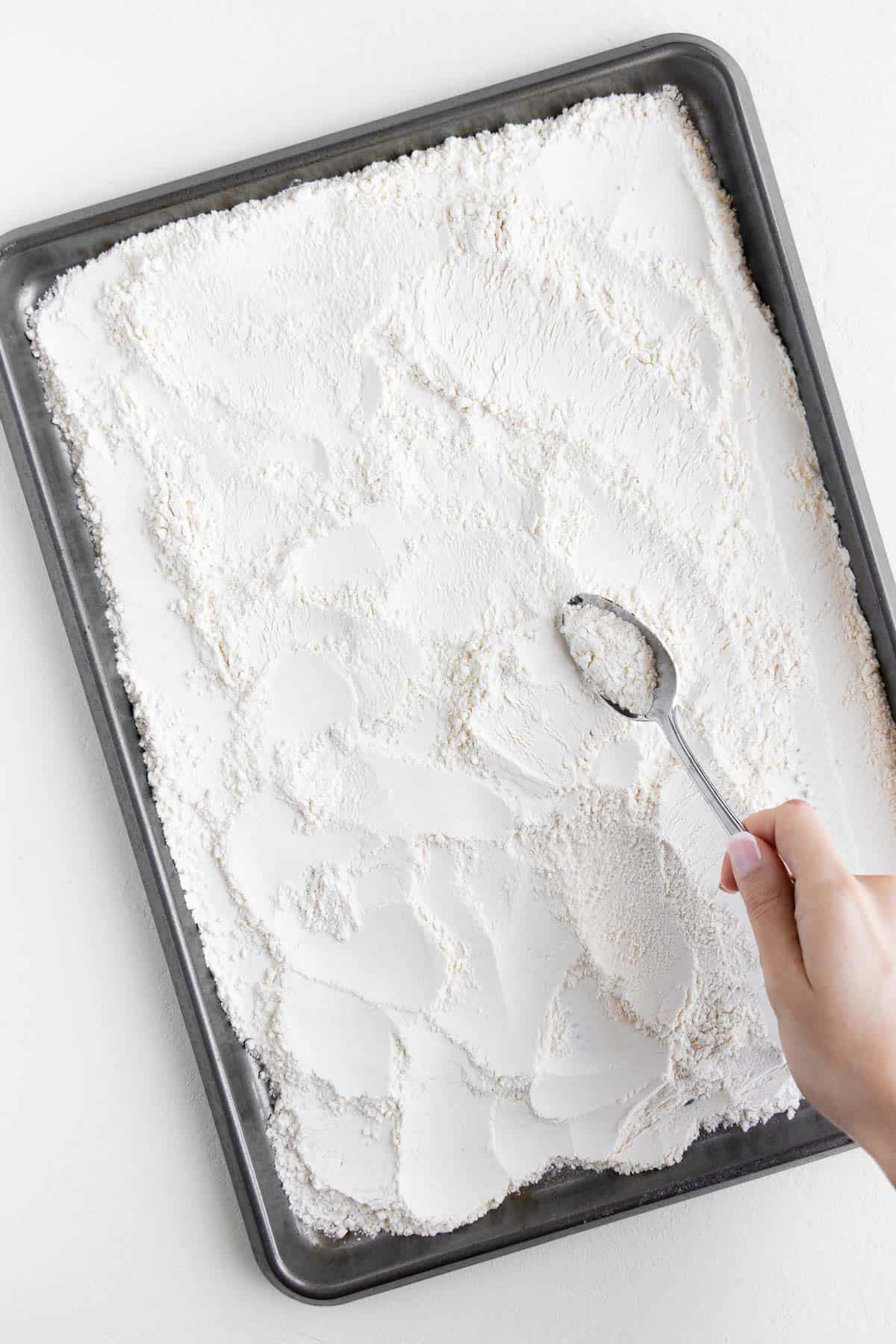 a hand spreading all-purpose flour onto a metal baking sheet