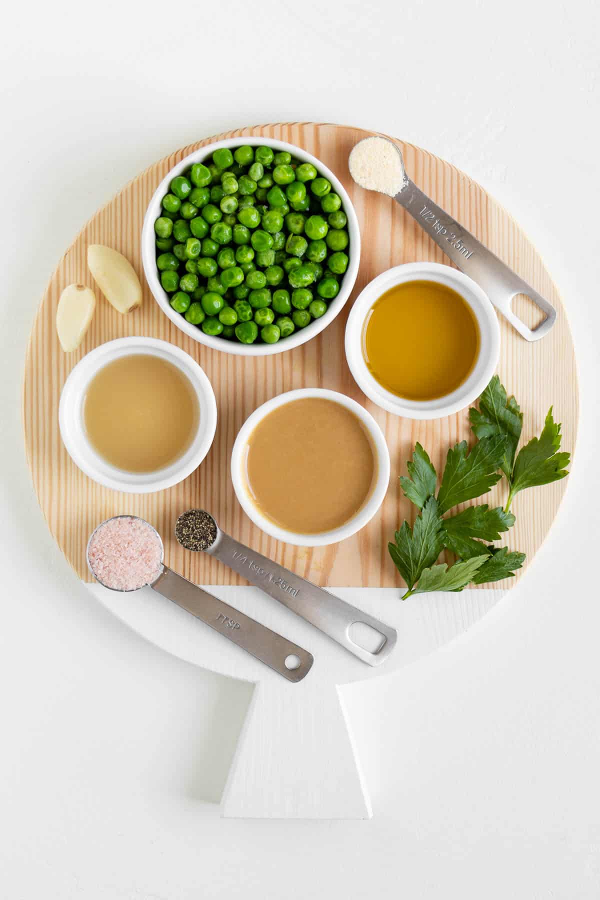 a circular wood cutting board topped with lemon juice, parsley, olive oil, tahini, garlic, peas, salt, and pepper