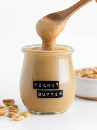 a wooden spoon scooping homemade peanut butter out of a small glass jar