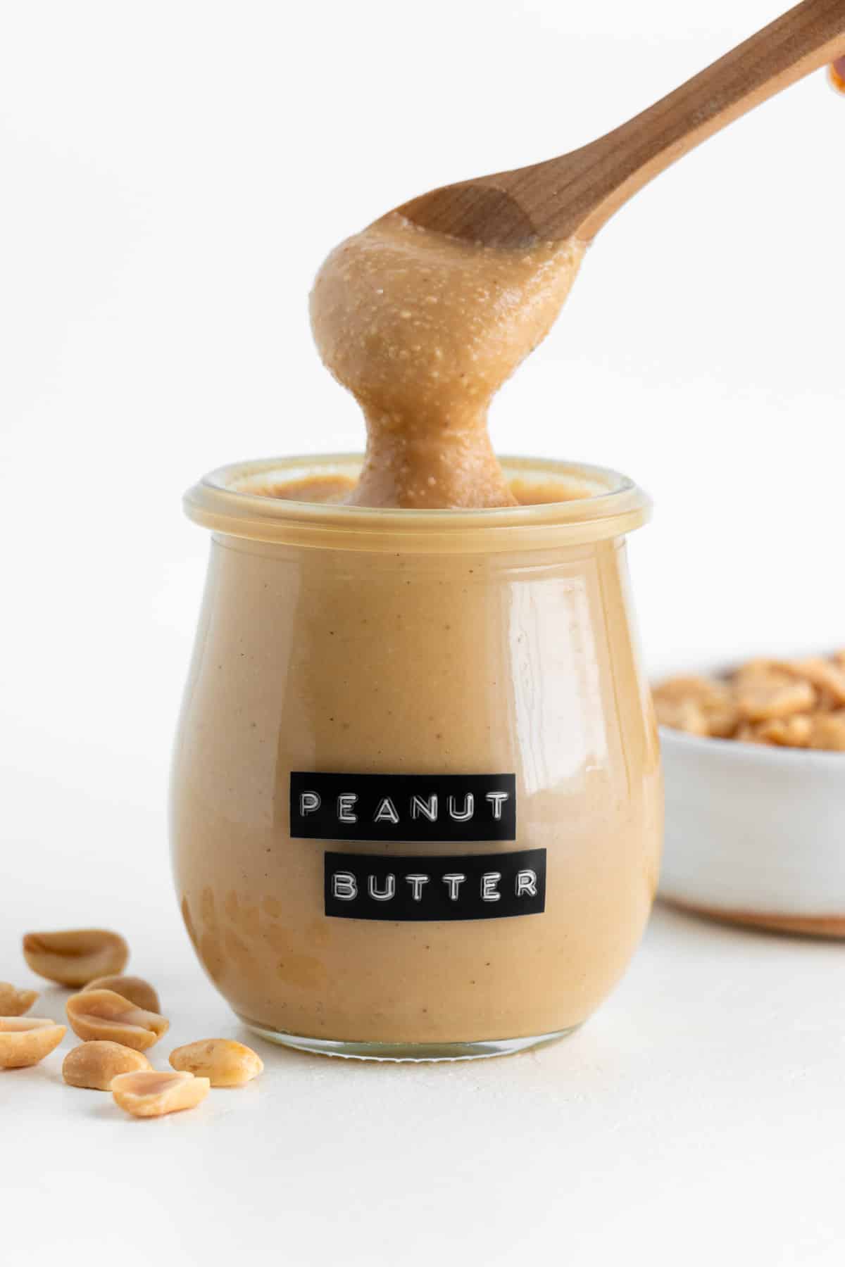 a wooden spoon scooping homemade peanut butter out of a small glass jar
