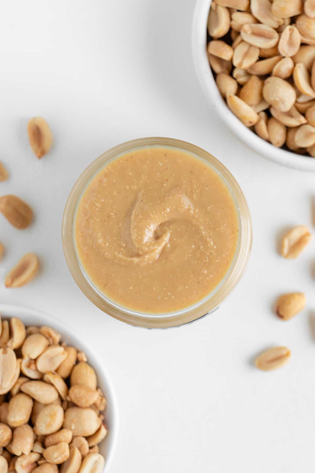creamy peanut butter inside a glass jar surrounded by chopped peanuts