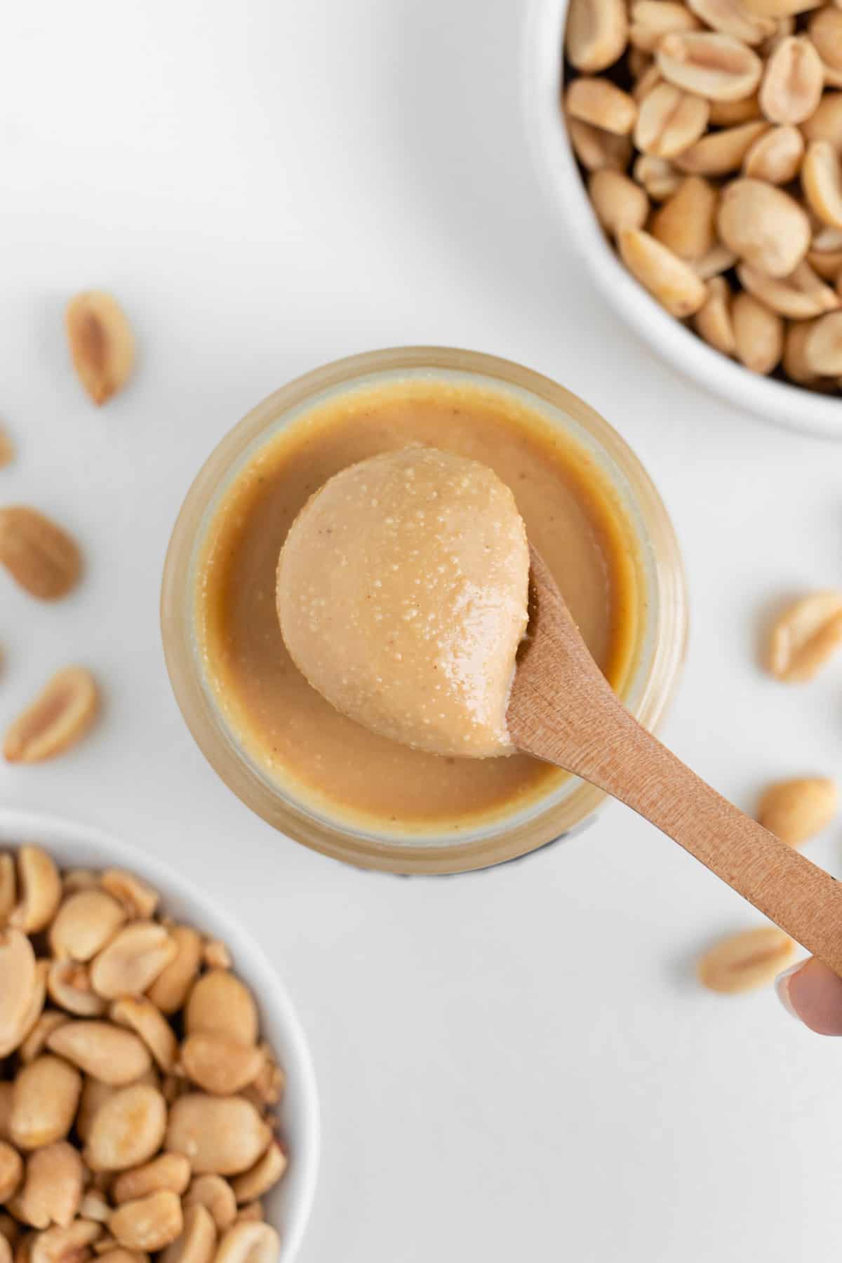 a wooden spoon scooping into a glass jar of nut butter