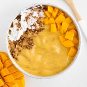 a mango turmeric smoothie bowl alongside a bamboo spoon and sliced mango