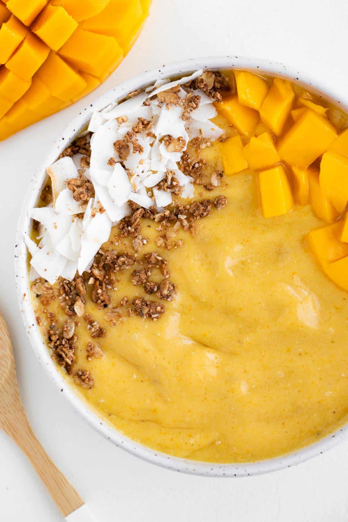 a bright yellow smoothie inside a bowl topped with coconut and granola