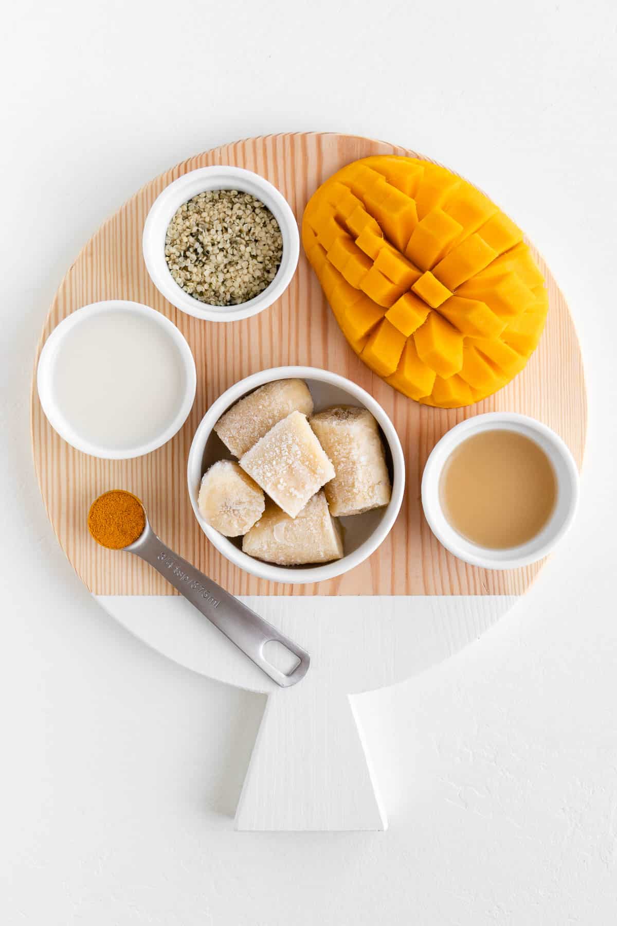 a round wooden cutting board topped with fruit, lemon juice, turmeric powder, hemp seeds, and coconut milk