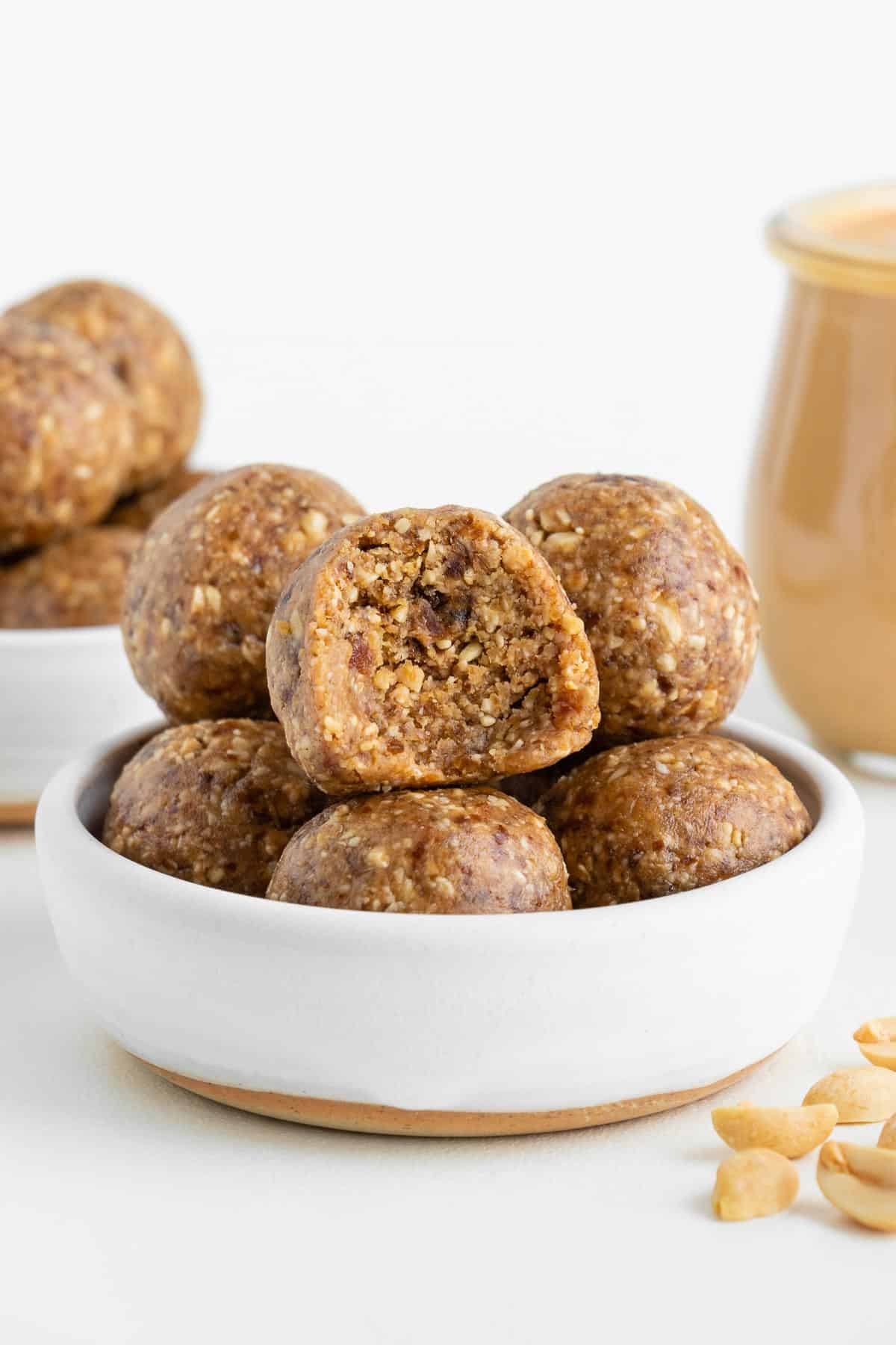 peanut butter energy balls stacked inside a white ceramic bowl with a bite taken out of the center ball