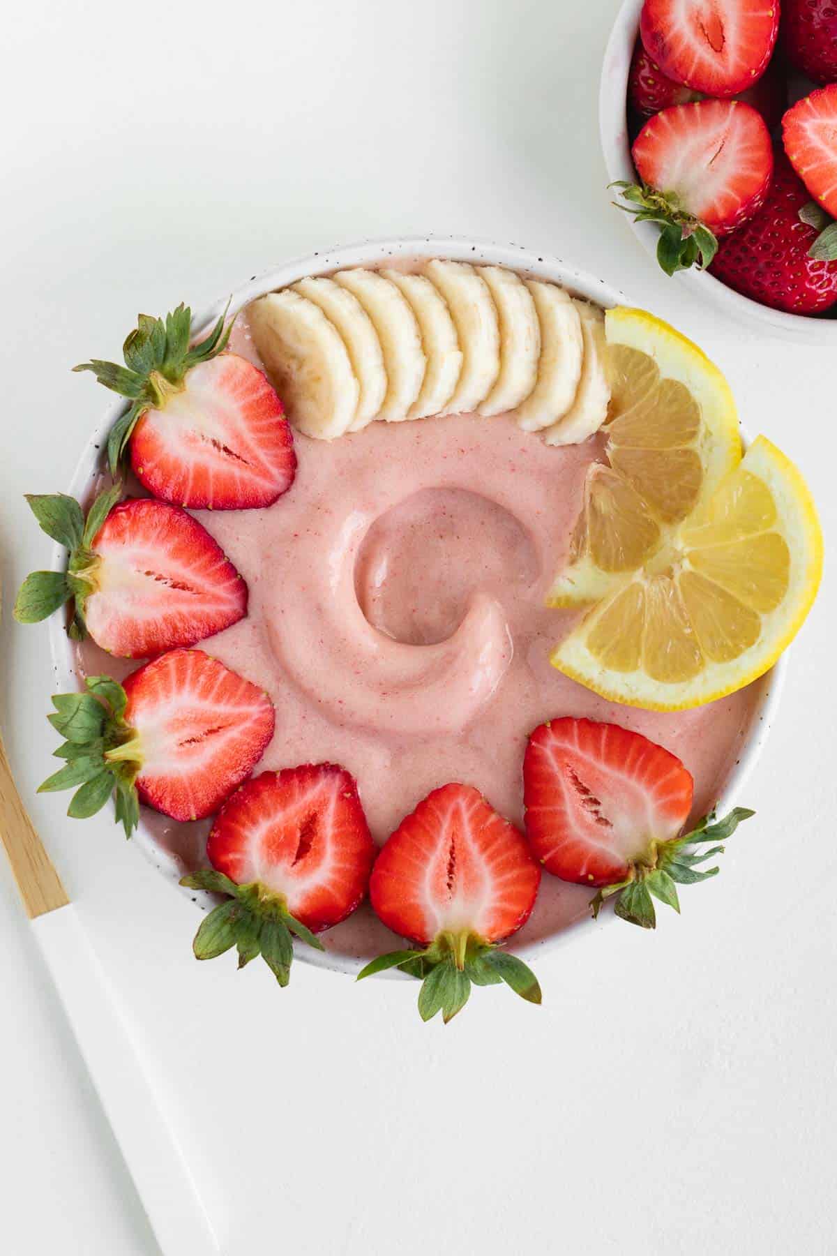 a strawberry lemonade smoothie inside a bowl topped with banana, berries, and sliced lemon