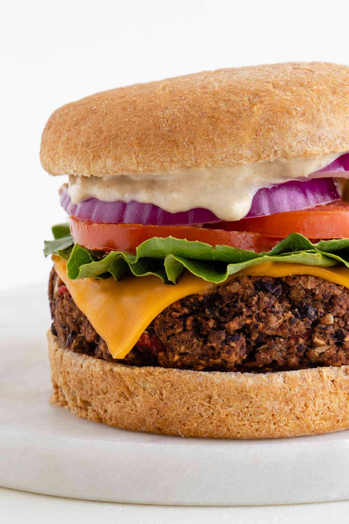 vegan black bean burger stacked with lettuce, tomato, red onion, pickled jalapeño, vegan cheese, and mayo