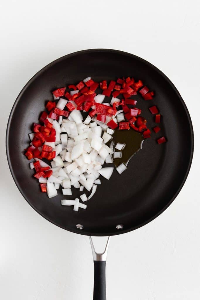 red bell pepper, onion, and olive oil on a black frying pan