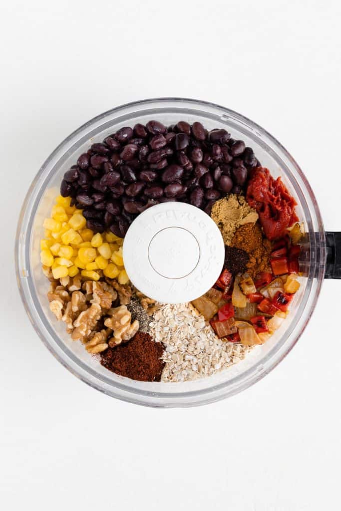 black beans, walnuts, corn, peppers, onions, oats, and spices inside the bowl of a food processor